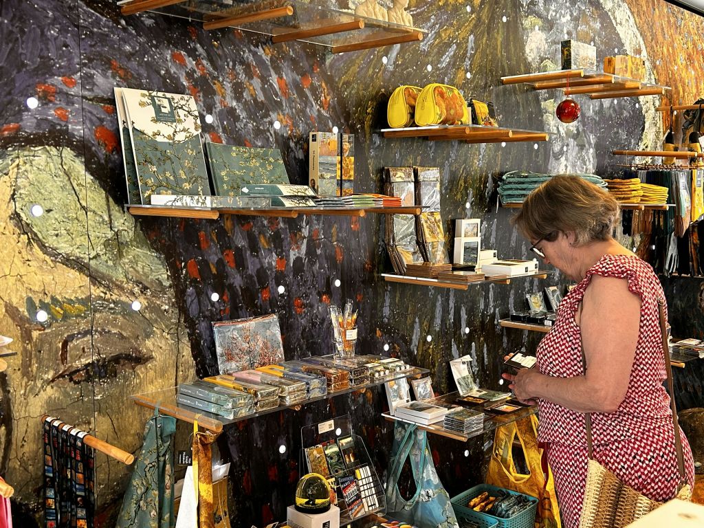 다채로운 색상의 선반과 진열된 상품이 있는 매장에서 미술 용품과 선물을 판매하는 빨간색 체크무늬 드레스 상점을 운영하는 여성입니다.