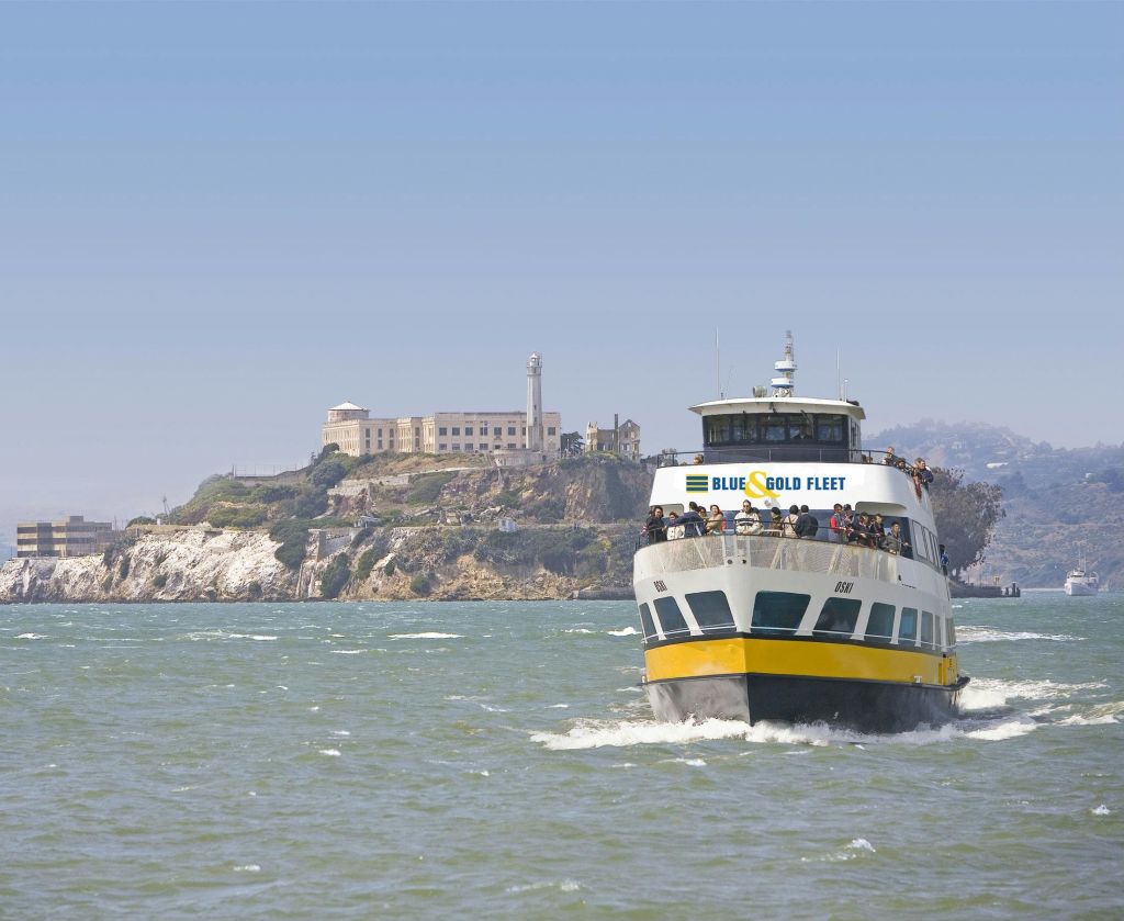 "Blue & Gold Fleet" 이라는 이름의 페리가 섬과 유서 깊은 건물을 배경으로 접근합니다.