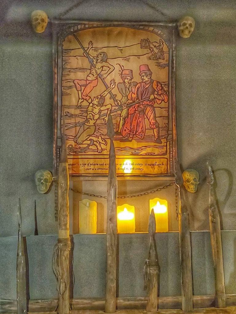 두개골, 창, 불이 켜진 촛불이 그 아래에 놓인 전투 장면을 묘사한 오래된 일러스트입니다.