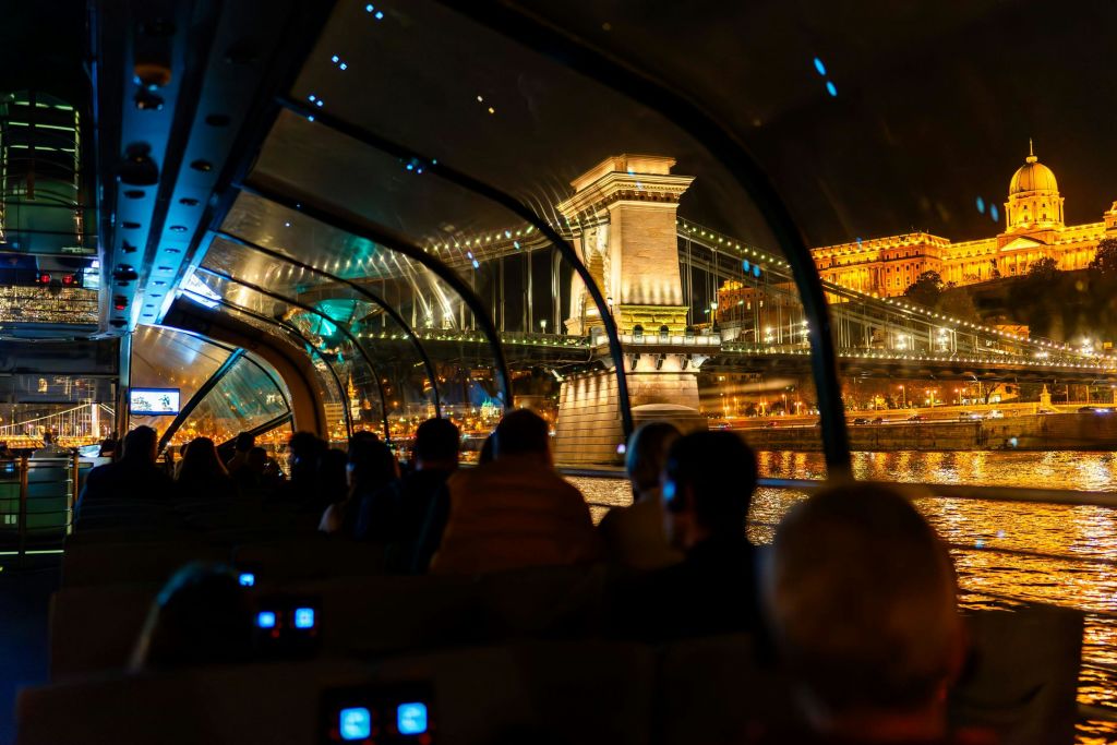 야간에 불이 켜진 다리와 도시 풍경을 감상할 수 있는 유리 지붕의 보트 내부.