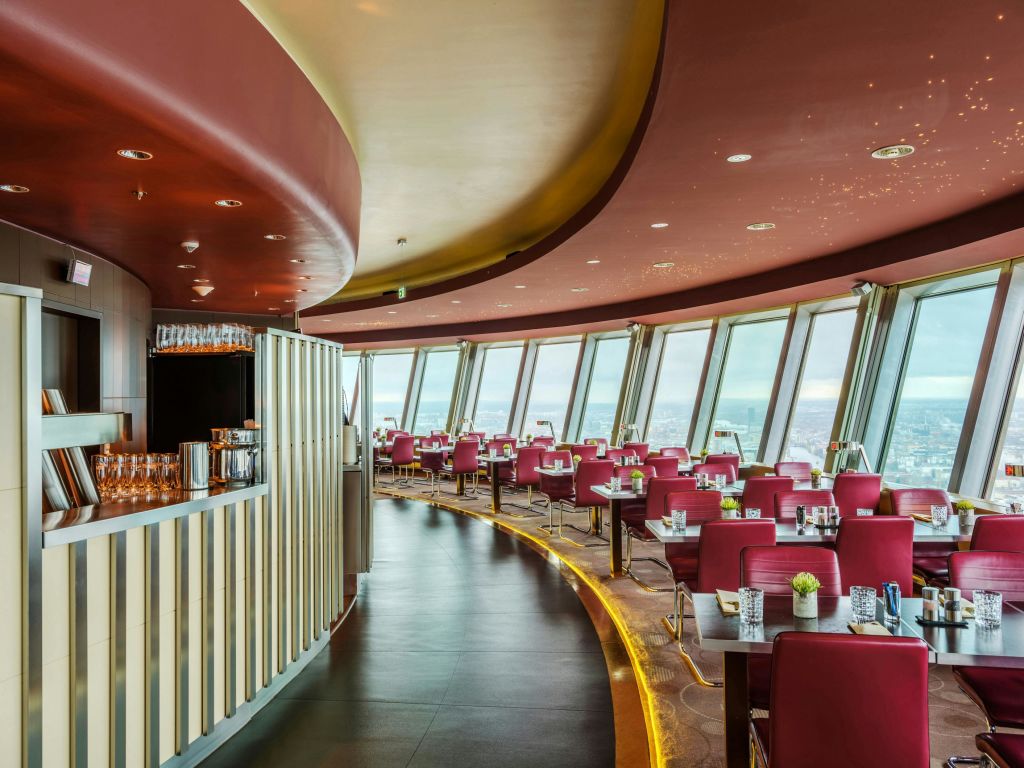 커다란 창문, 빨간 의자, 세련된 바 공간을 갖춘 현대적이고 고급스러운 레스토랑으로 도시 풍경을 파노라마로 감상할 수 있습니다.