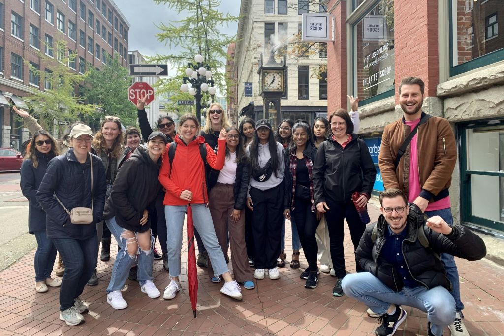 한 무리의 사람들이 증기시계 근처의 자갈길과 도시 지역의 정지 표지판에서 사진을 찍기 위해 포즈를 취하고 있습니다.