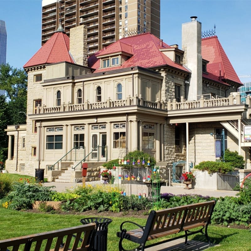 붉은 지붕, 나무 벤치, 잘 손질된 정원, 고층 건물을 배경으로 한 유서 깊은 석조 건물.