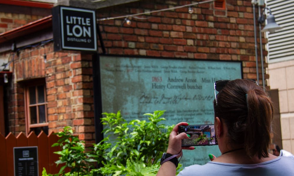 녹음으로 둘러싸인 벽돌 벽에 "Little Lon Distilling Co." 표지판을 촬영한 사람.