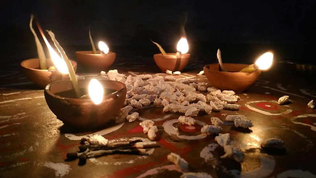 흰색 질감의 조각으로 둘러싸인 장식된 표면에 불타는 심지가 있는 4개의 점토 오일 램프.