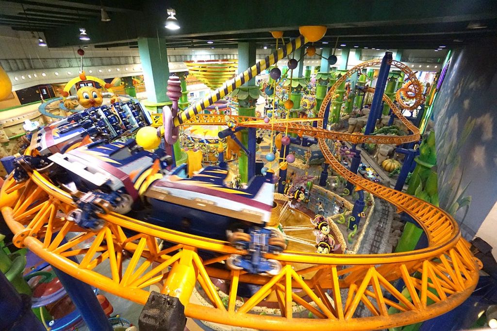 다채로운 색상의 롤러코스터, 테마 장식, 아케이드 게임이 있는 실내 놀이공원.