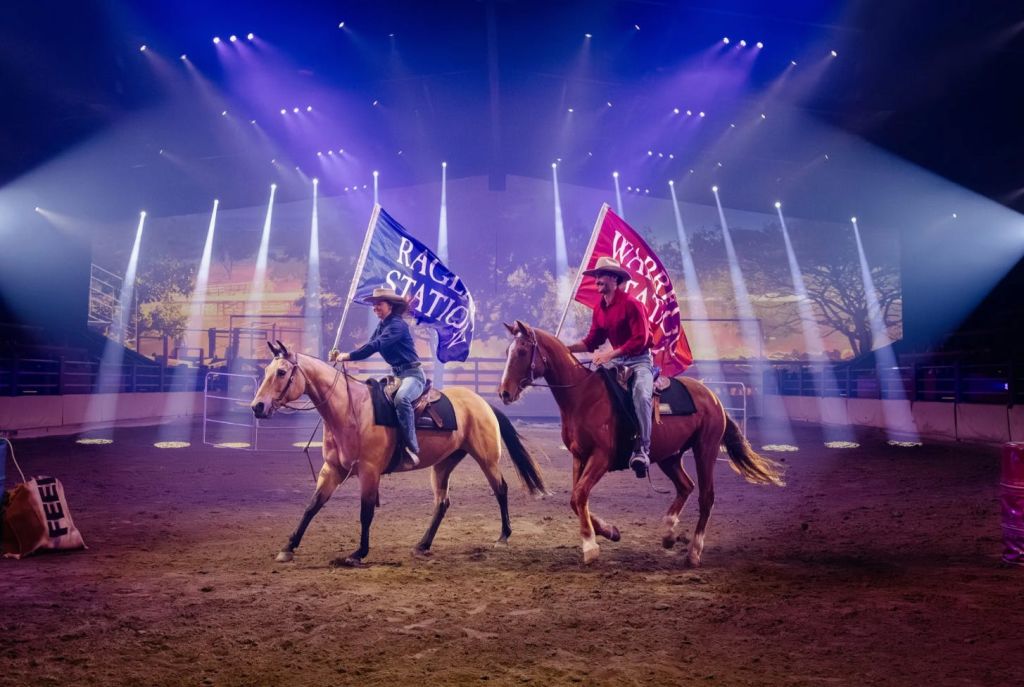 실내 경기장에서 말을 탄 두 명의 승객이 밝은 무대 조명이 있는 '래글런 스테이션' 과 '월드' 라고 적힌 깃발을 들고 있습니다.
