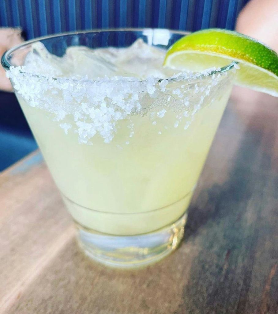 소금 테두리와 라임 웨지 장식이 있는 유리잔의 마가리타가 나무 테이블 위에 놓여 있습니다.