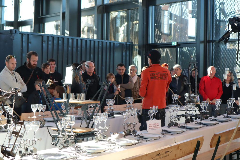 사람들은 실내에 모여 기계식 금기 사항과 유리 공예품을 갖춘 정교한 테이블이 놓인 시연을 지켜보았습니다.