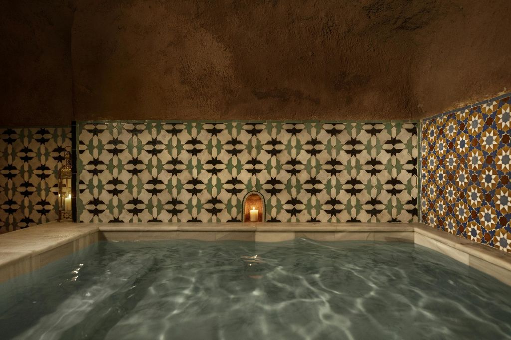 무늬가 있는 벽이 있는 타일로 마감된 실내 수영장, 조명이 켜진 촛불을 들고 있는 작은 틈새, 물 반사.