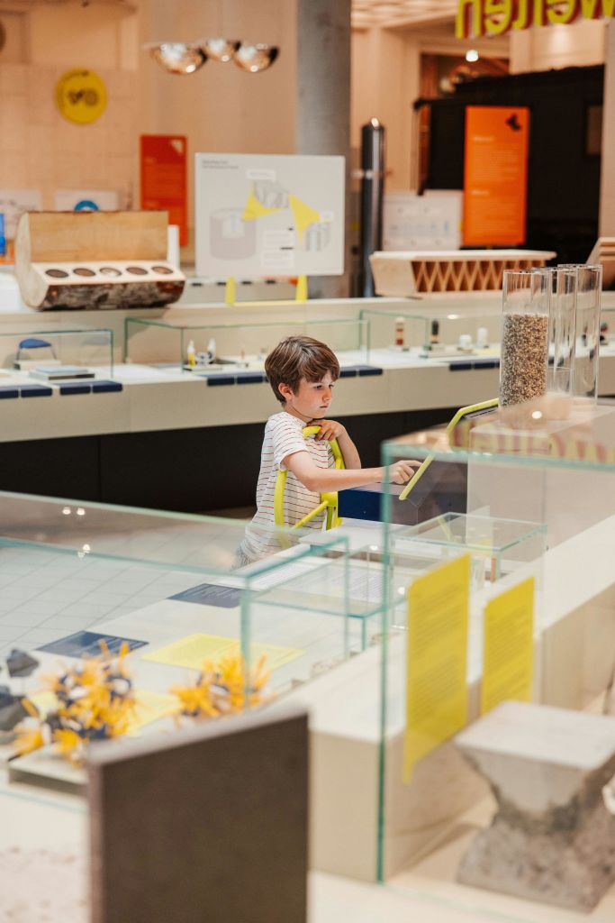 한 어린이가 다양한 디스플레이와 정보 패널로 둘러싸인 과학 박물관의 전시물과 상호 작용합니다.
