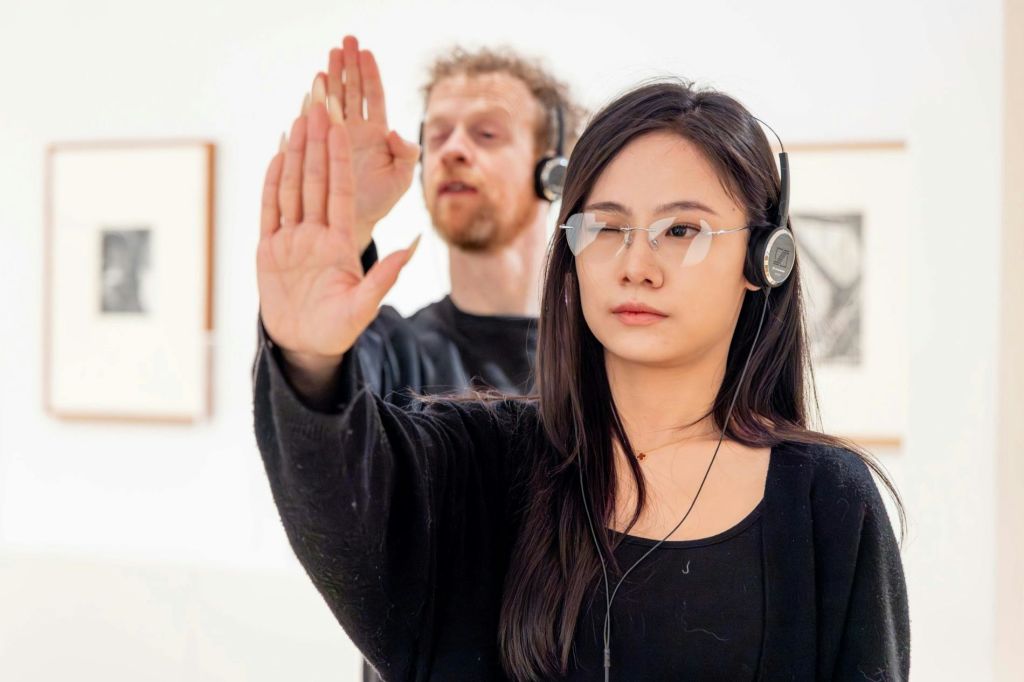 헤드폰을 착용하고 안경을 쓴 두 사람이 가벼운 실내 환경에서 제스처로 손을 들고 있습니다.