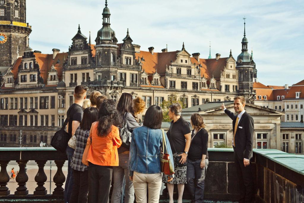 투어 가이드는 한 무리의 사람들이 세심하게 듣고 같은 방향을 바라보며 화려한 역사 건물을 가리킵니다.