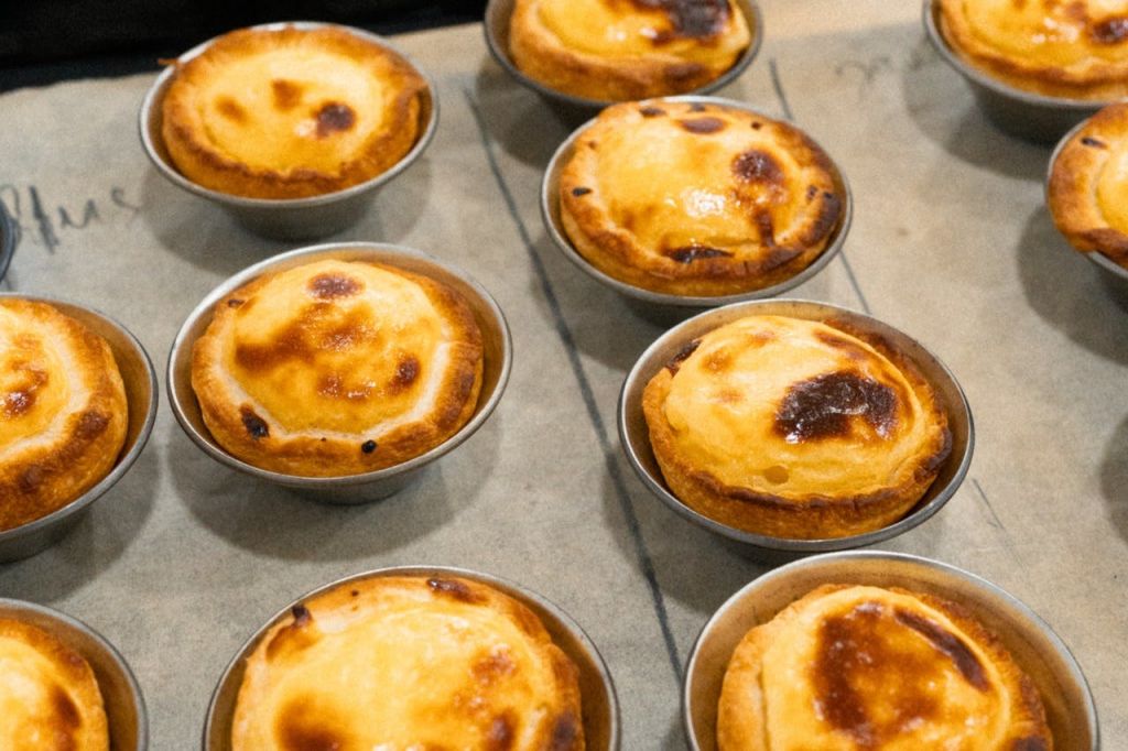 베이킹 트레이의 개별 금속 몰드에 금빛 갈색 상판이 달린 여러 구운 커스터드 타르트.