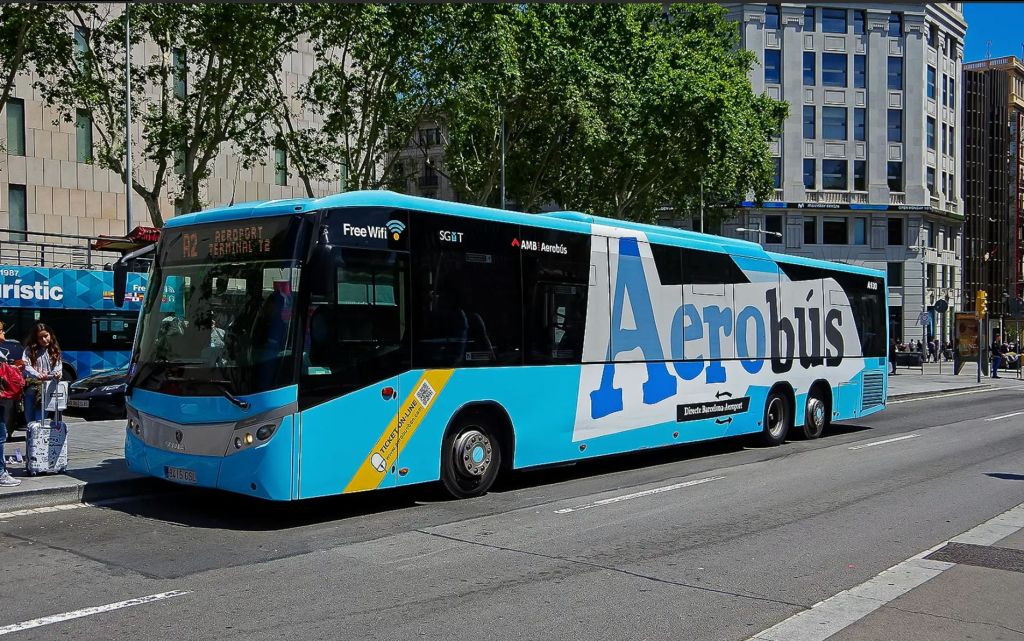 "Aerobús" 라고 표시된 파란색과 흰색 버스가 거리에 주차되어 있으며, 건물과 나무를 배경으로 무료 와이파이를 제공합니다.