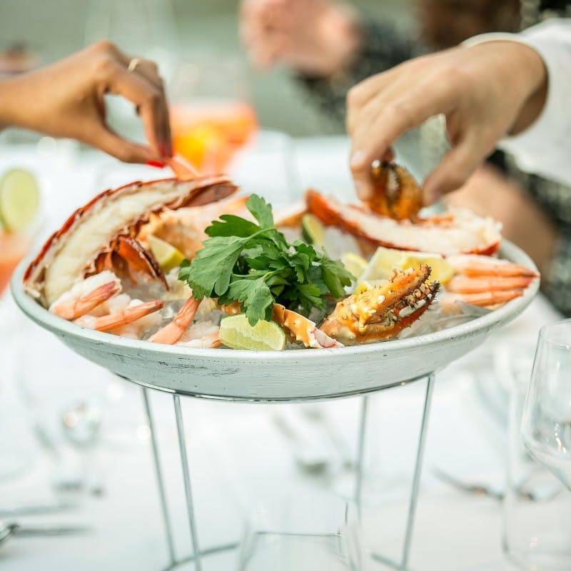 바닷가재, 새우, 장식이 들어간 해산물 접시로, 두 사람이 식사 테이블에서 직접 서빙합니다.