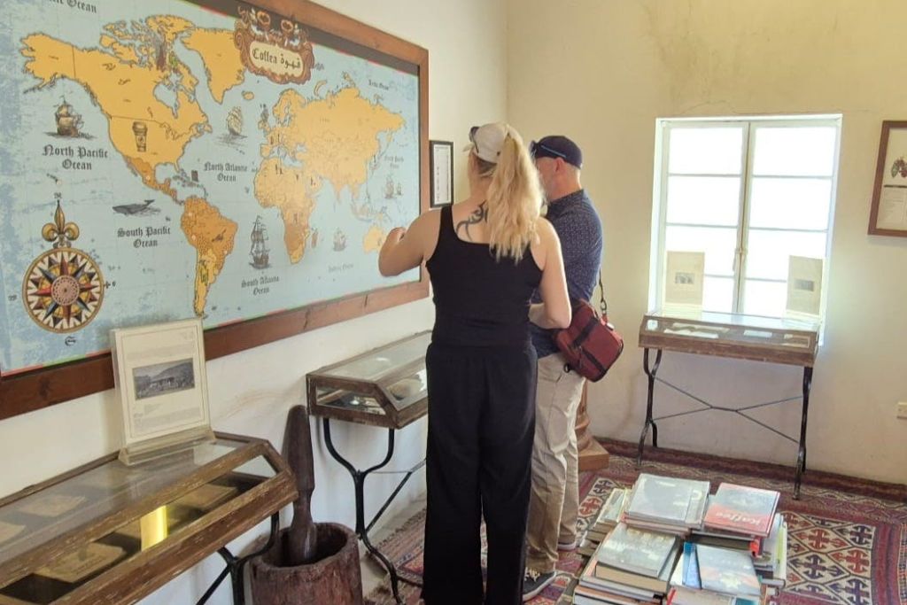 두 사람이 작은 방에 서서 벽에 놓인 커다란 지도를 살펴보고 있습니다. 방에는 진열 케이스와 흩어져 있는 책이 있습니다.