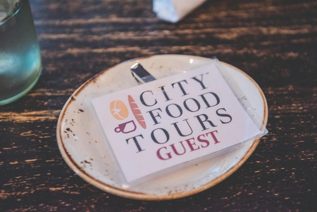 '시티 푸드 투어 게스트' 라는 이름표가 나무 테이블 위에 놓인 흰색 접시 위에 놓여 있습니다.