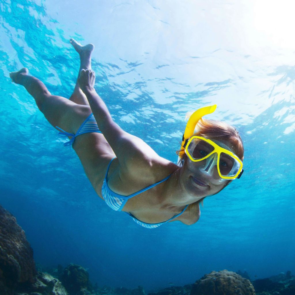 푸른 물과 산호로 둘러싸인 노란색 마스크로 수중에서 줄무늬 수영복 스노클링을 하는 사람.