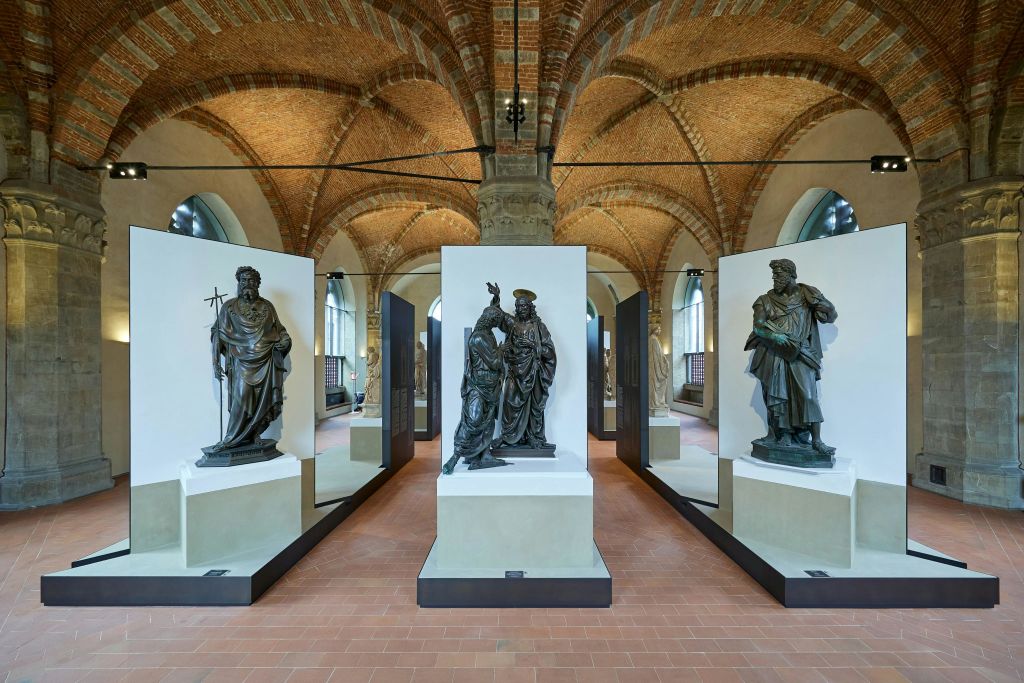 미술관을 배경으로 받침대, 아치형 벽돌 천장, 석조 기둥에 조각상이 전시된 전시 공간입니다.