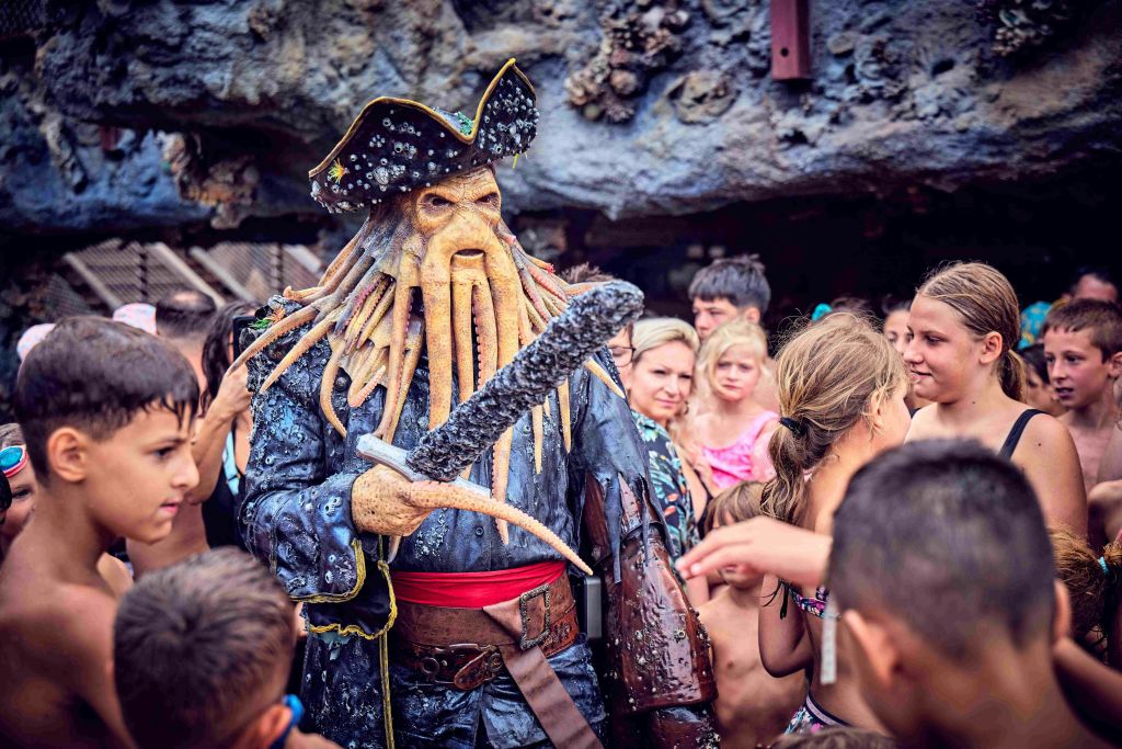 촉수 기능이 있는 해적 의상을 입은 사람은 혼잡한 야외 환경에서 어린이 그룹과 상호 작용합니다.