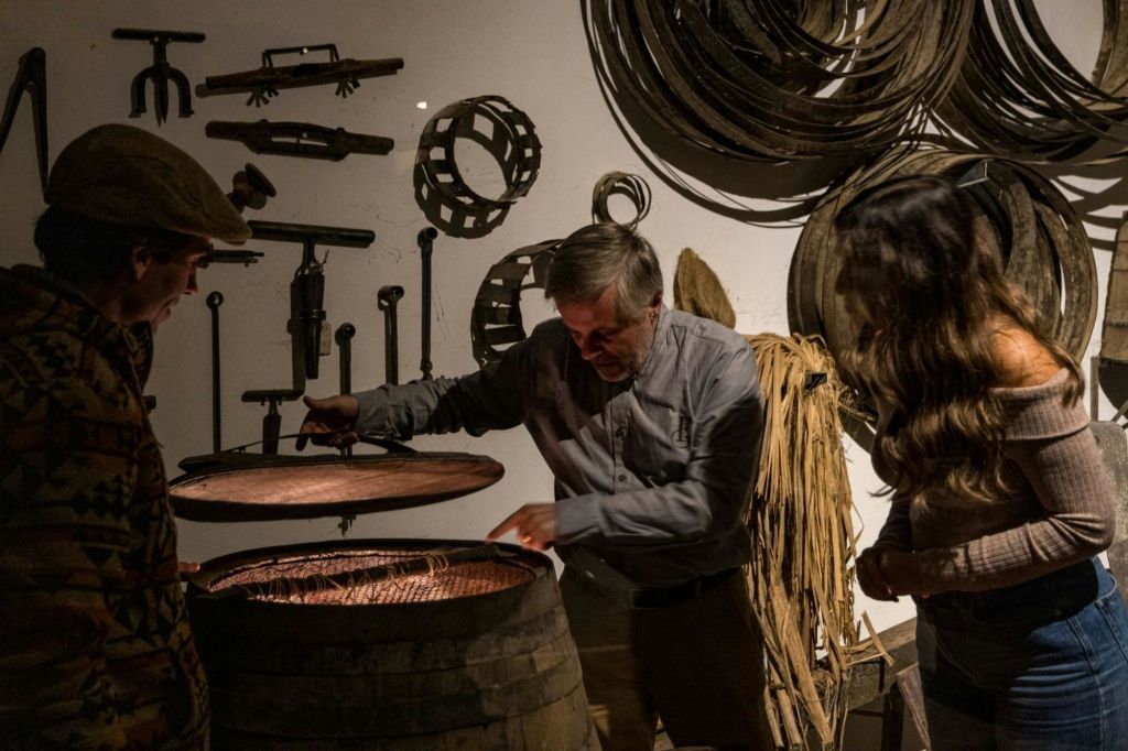 세 사람이 벽에 도구, 바퀴 및 기타 장비가 있는 방의 나무 통 내부를 살펴보고 있습니다.