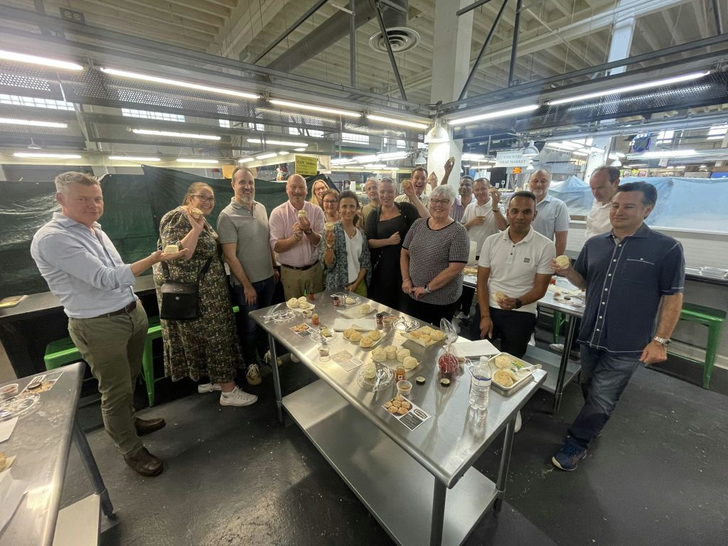 인더스트리얼한 분위기의 다양한 음식이 놓인 금속 테이블 주위에 서 있는 사람들의 모임.