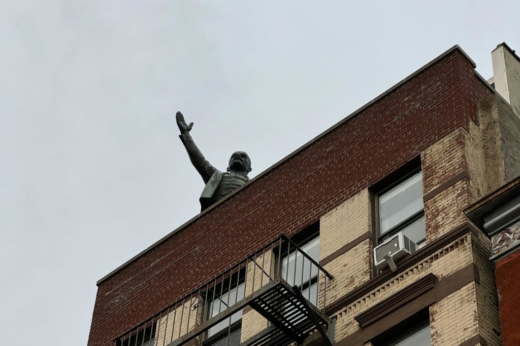 벽돌 건물 옥상에서 불이 튀어나와 창문을 통해 들어올린 팔을 뻗고 있는 사람의 동상.
