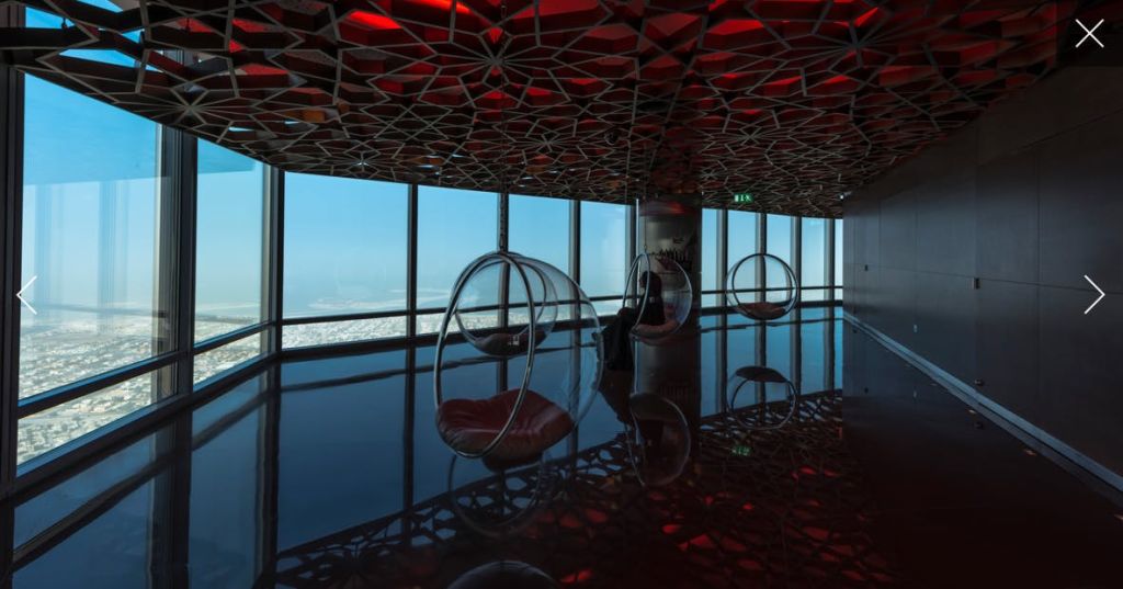 바닥에서 천장까지 이어지는 창문에 매달린 거품 의자, 복잡한 천장, 탁 트인 바다 전망을 갖춘 현대적인 라운지.