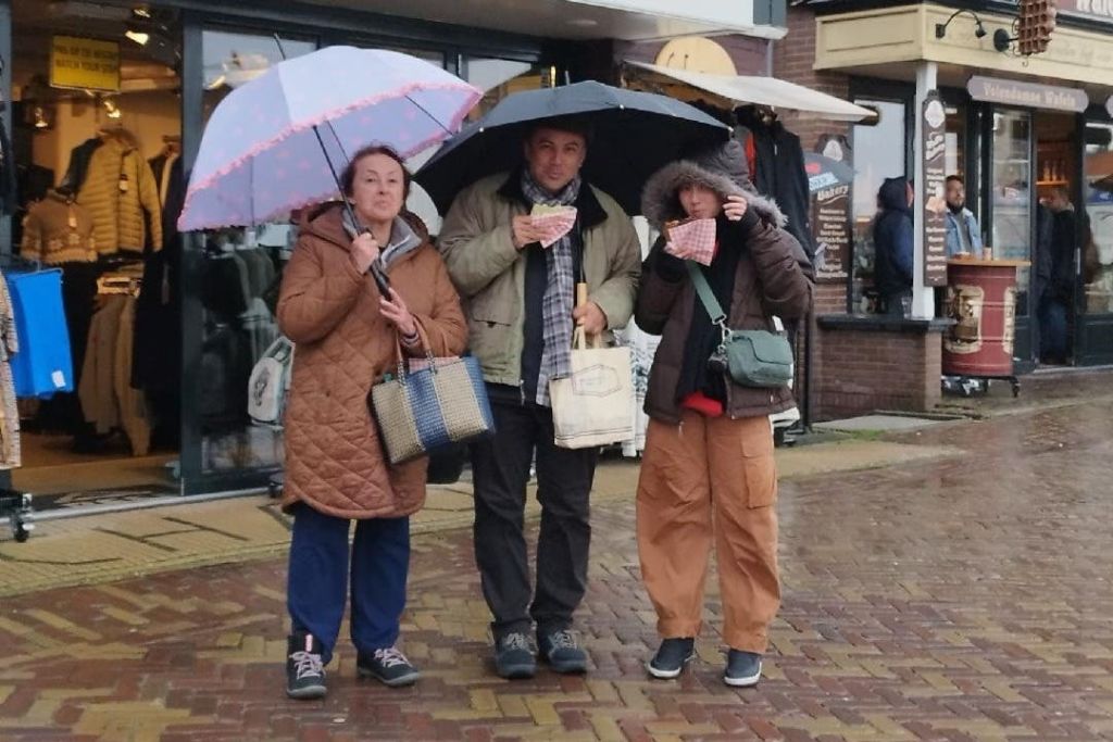 젖은 포장 도로에 있는 옷가게 앞에서 우산 아래 서 있는 세 사람.