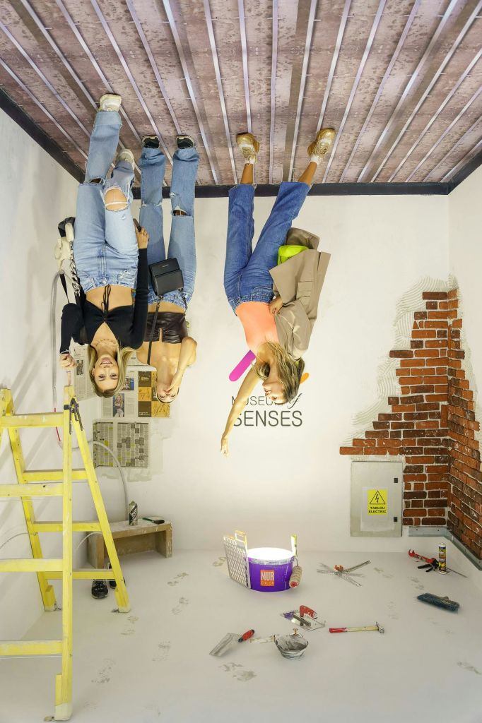 건축 도구와 벽돌 벽이 있는 방에 세 사람이 거꾸로 서 있는 것 같습니다.