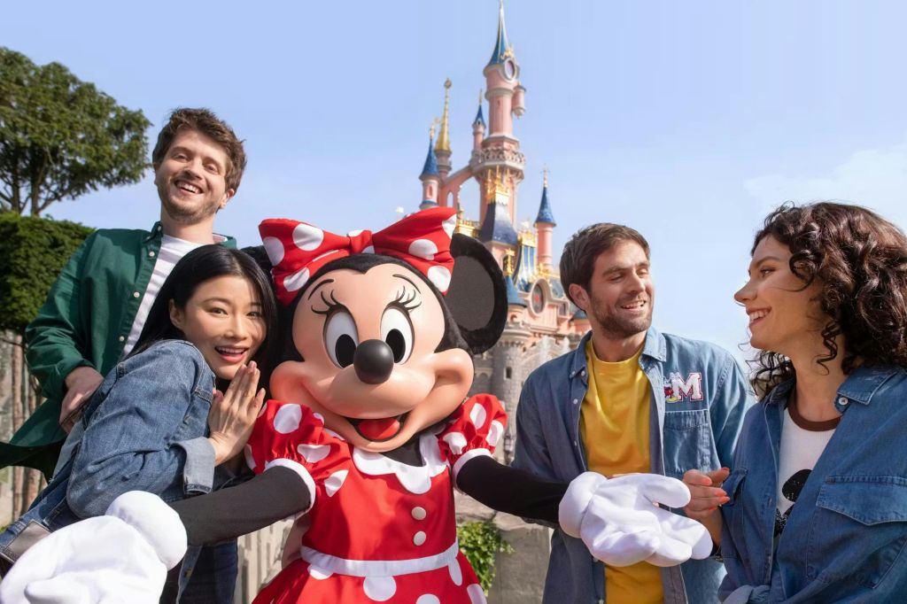 한 무리의 사람들이 맑고 푸른 하늘 아래 성 앞에서 미니마우스와 함께 미소를 짓고 있습니다.