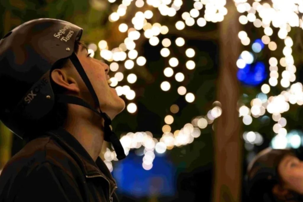 밤에 나무에 흐릿하고 빛나는 불빛을 배경으로 헬멧을 쓴 사람이 위를 바라보고 있습니다.