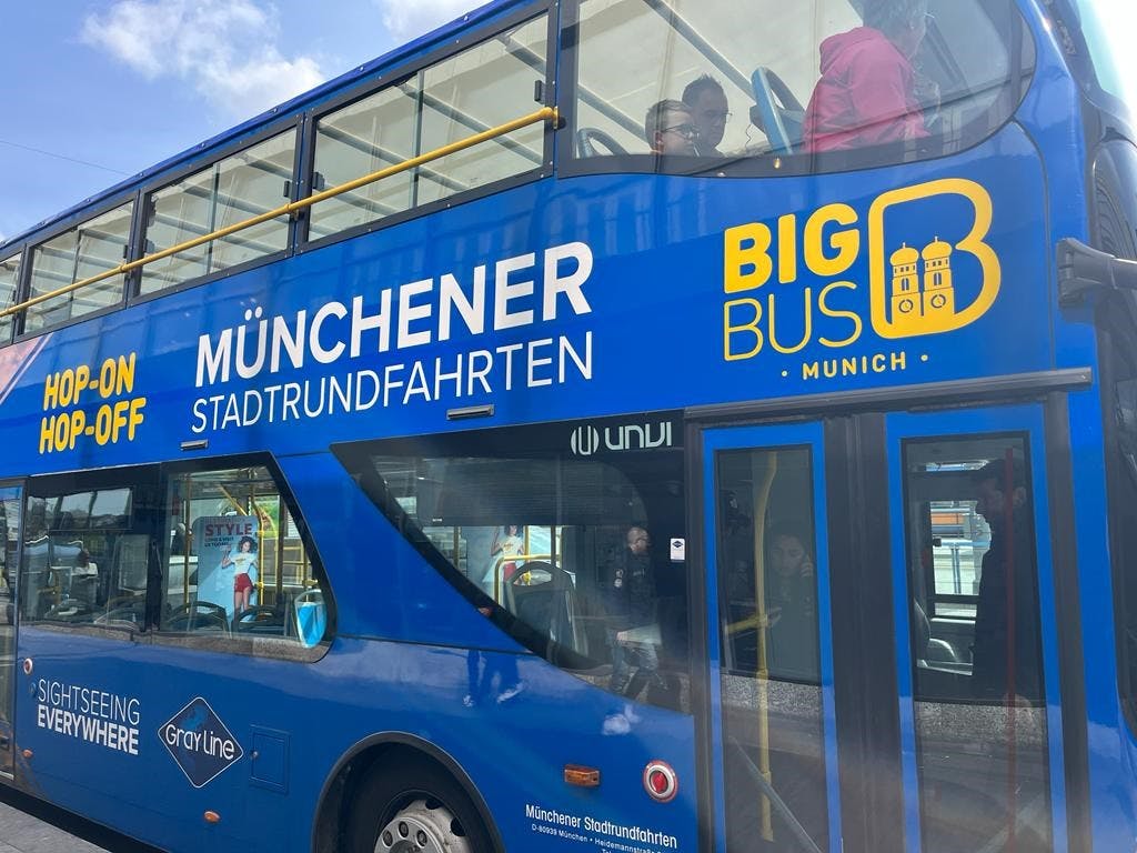 "Münchener Stadtrundfahrten" 과 "Big Bus Munich" 로고가 있는 뮌헨의 파란색 2층 투어 버스가 정류장에 주차되어 있습니다.