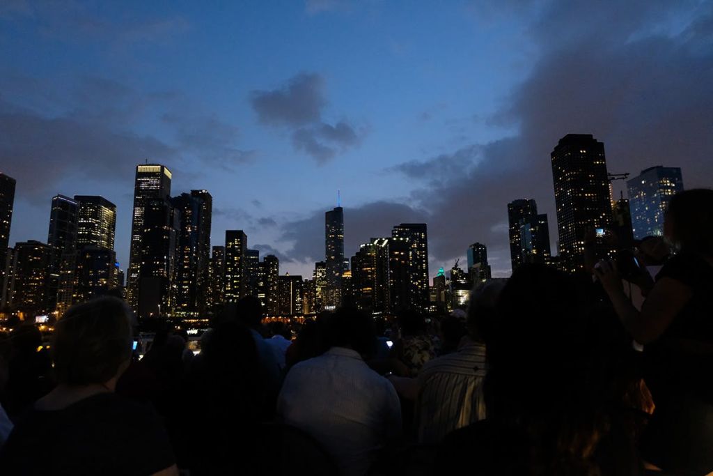 사람들은 해질녘 야외에 앉아 부분적으로 흐린 하늘 아래 빛나는 고층 건물로 도시의 스카이라인을 배경으로 실루엣을 꾸몄습니다.