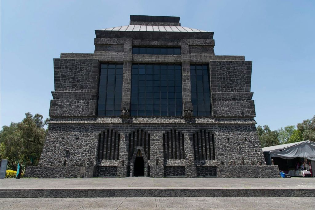 맑고 푸른 하늘 아래, 직사각형 창문과 아치형 입구가 있는 커다란 석조 건물.