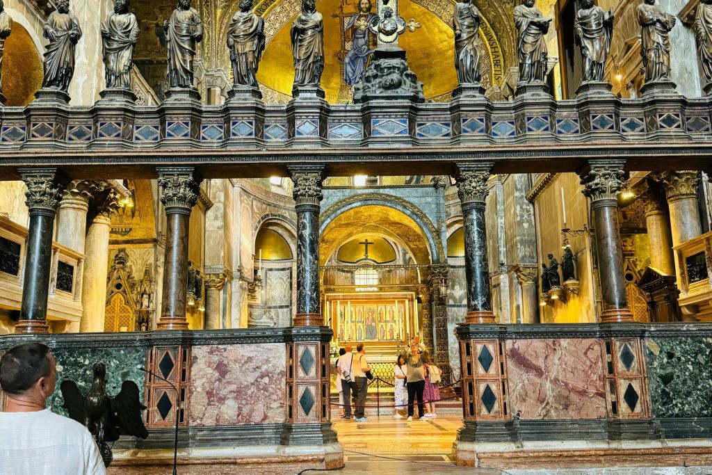 조각상, 아치, 사람들이 정교한 장식 아래 황금 제단을 바라보고 있는 화려한 교회 내부.