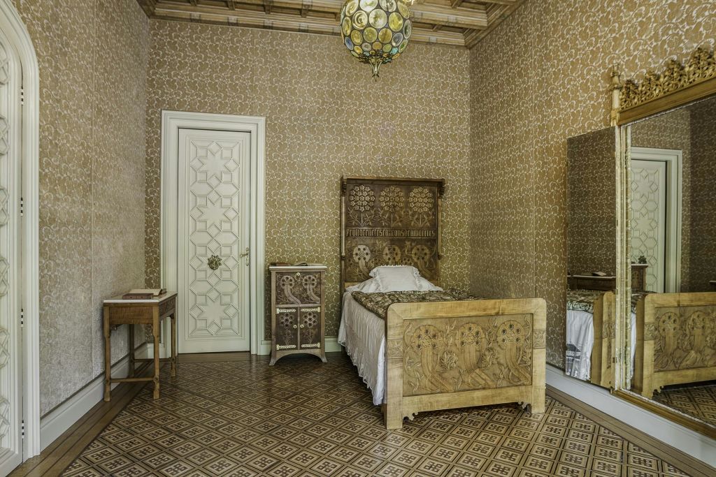 무늬가 있는 벽지, 원목 침대, 침대 협탁, 작은 테이블, 거울 옷장, 타일 바닥이 있는 화려한 침실.
