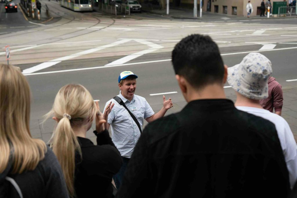 파란색 모자와 흰색 셔츠를 입은 남성이 도시 거리 모퉁이에서 소규모 그룹과 이야기하면서 활기차게 제스처를 취하고 있습니다.