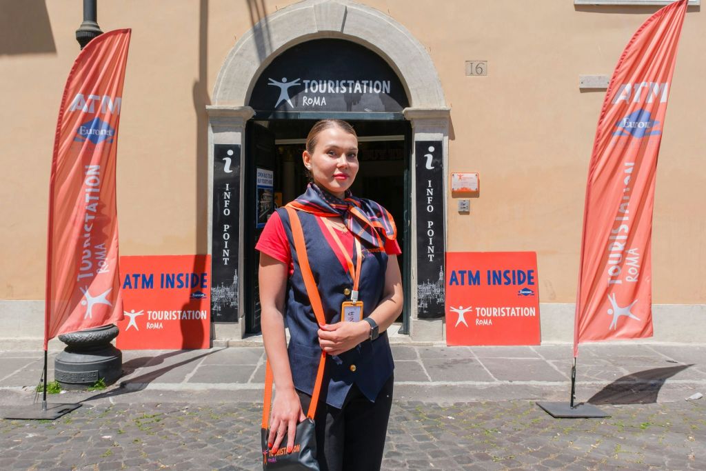 제복을 입은 여성이 'ATM Inside' 와 'Touristation Roma' 표지판이 있는 관광 안내소 앞에 서 있습니다.