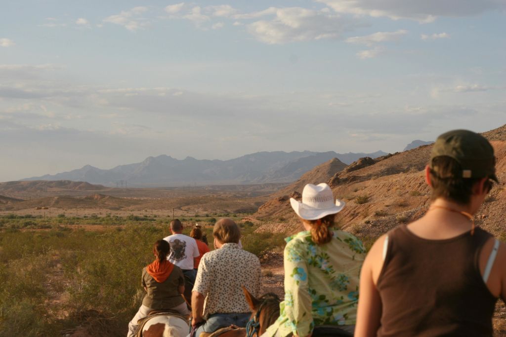 부분적으로 흐린 하늘 아래 산을 배경으로 사막의 풍경을 감상하며 오솔길을 따라 말을 타는 사람들.