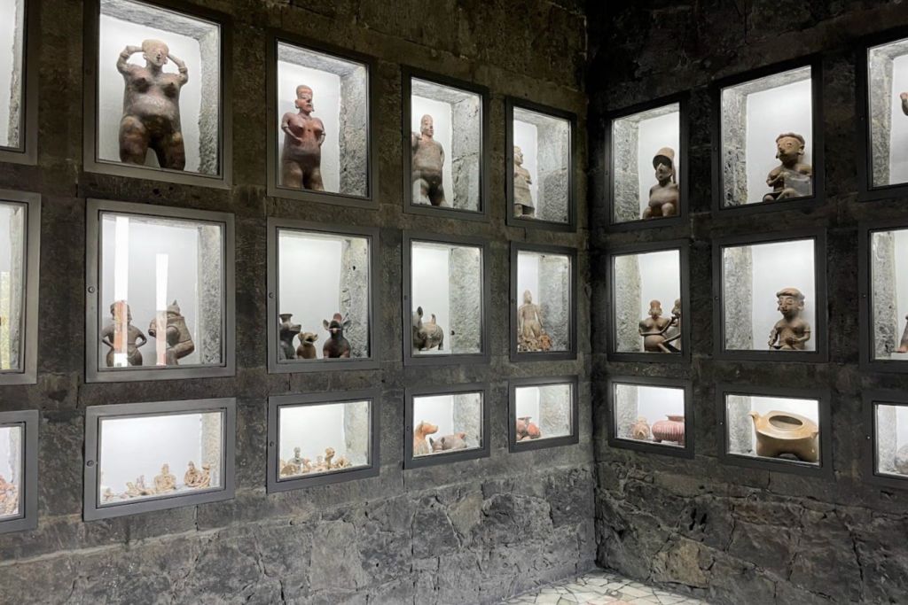 돌 구조물 안의 유리 상자에 있는 작고 고대로 보이는 인간 조각상의 벽면 디스플레이.