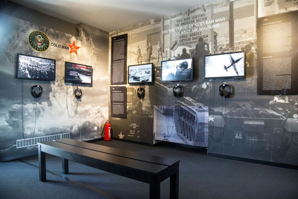 멀티미디어 스크린, 헤드폰, 정보 패널, 방문객을 위한 벤치를 갖춘 냉전 테마의 박물관 전시회.