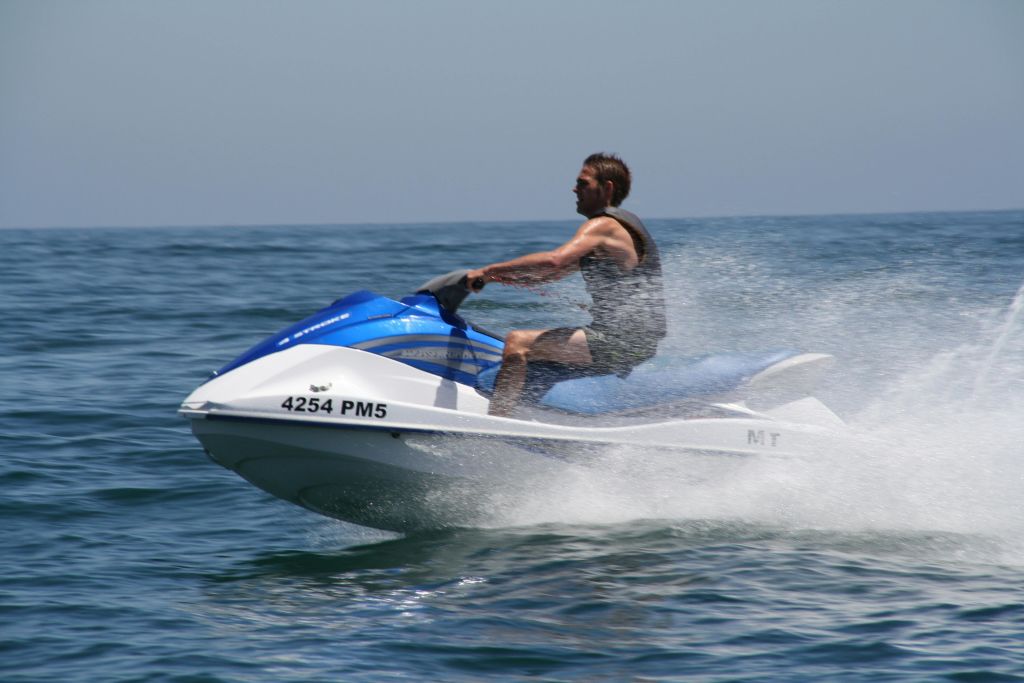 잔잔한 바다에서 파란색과 흰색 제트 스키를 타고 큰 물을 뿌리는 사람.