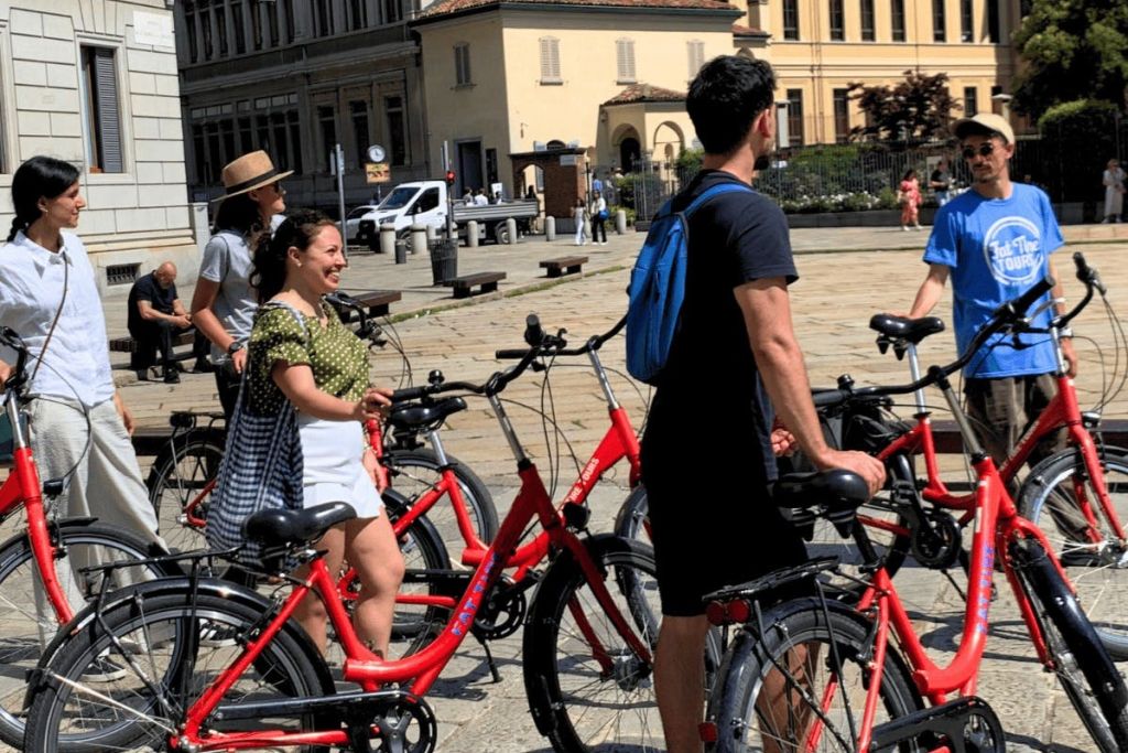 유서 깊은 건물을 배경으로 붉은 자전거를 탄 사람들이 광장에 서 있습니다.
