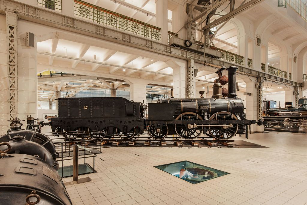 유서 깊은 증기 기관차는 조명이 밝고 넓은 박물관 내부에 전시되어 있으며, 건축학적 디테일과 유리 바닥 패널을 갖추고 있습니다.