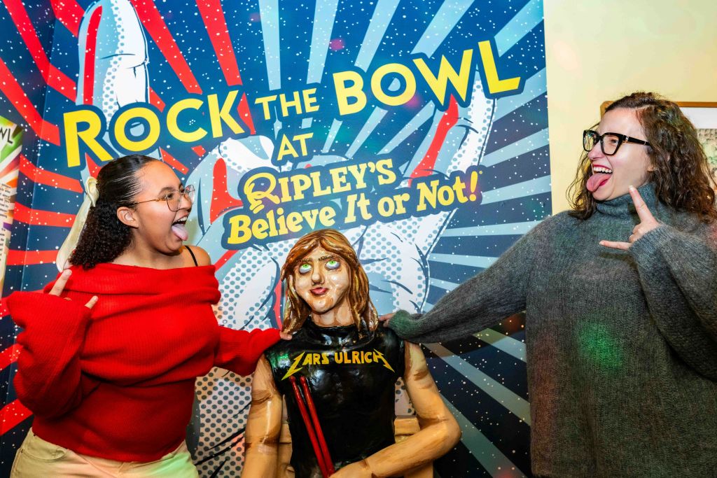 "Ripley's Believe It or Not!" 라고 적힌 표지판 앞에서 마네킹을 들고 혀를 내밀며 포즈를 취하는 두 여성