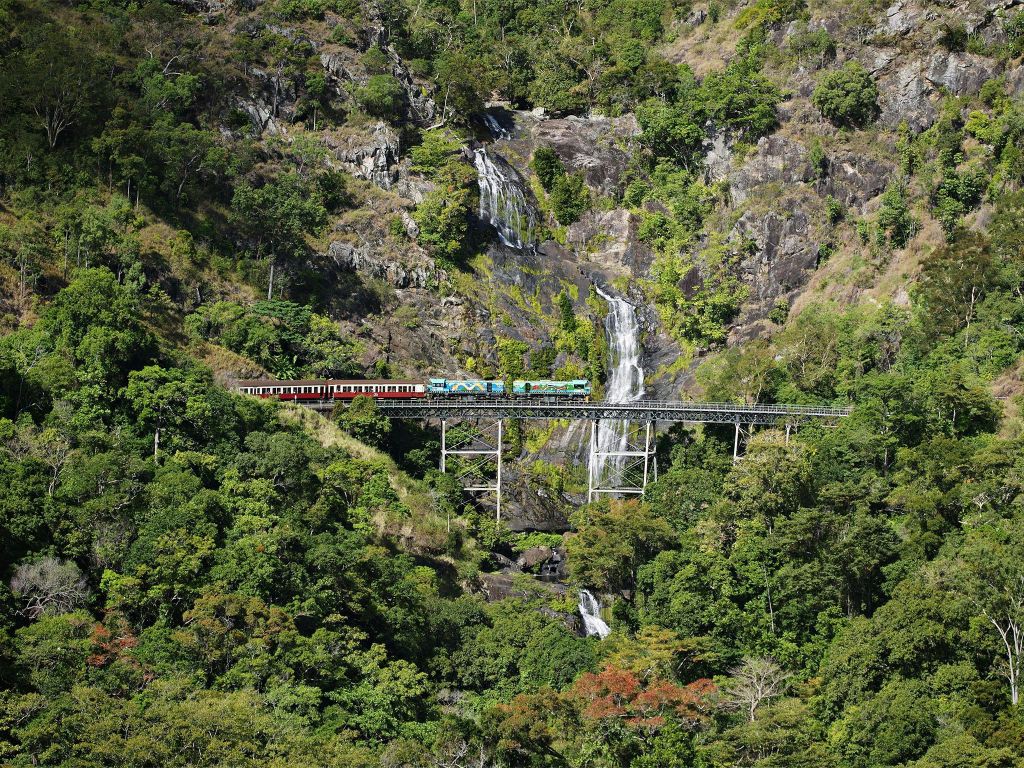 기차는 울창한 푸른 숲과 계단식 폭포로 둘러싸인 다리를 배경으로 이동합니다.