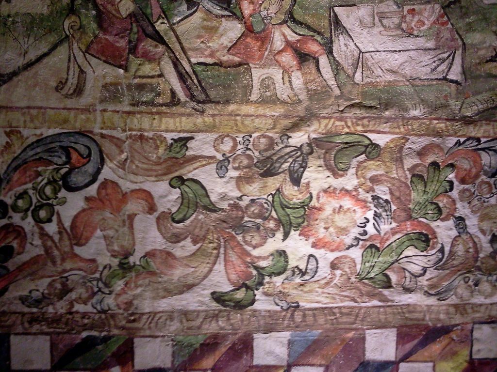 꽃 무늬, 기하학적 테두리, 테이블 주위의 피규어를 보여주는 화려하고 디테일한 프레스코화의 클로즈업입니다.