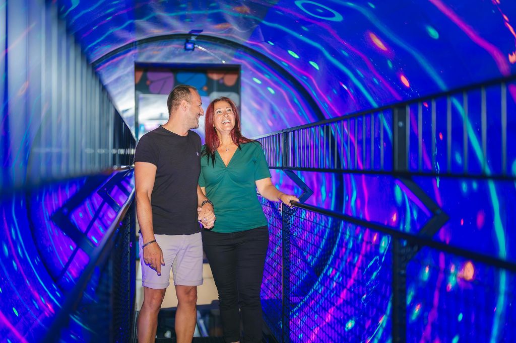 활기차고 다양한 색상의 조명이 있는 터널을 걸으며 손을 잡고 미소 짓는 커플.